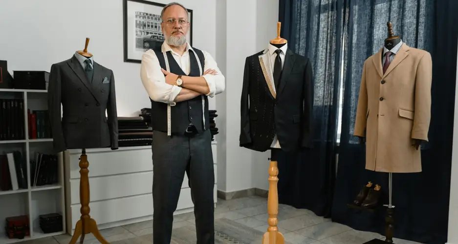 Älterer Herr mit verschränkten Armen steht in einem Raum zwischen drei Anzugpuppen.